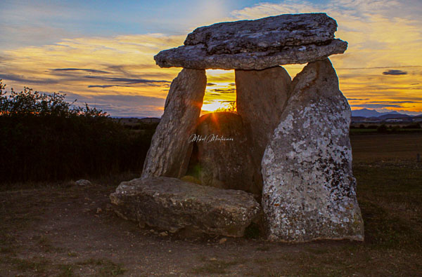 En esta foto del atardecer podemos ver podemos ver el brillante sol al fondo de la imagen por el hueco que tiene el dolmen de Sorginetxe que se encuentra en el plano medio un a un tercio del borde de la foto y como protagonista primer plano, por encima del sol hay algunas nubes teñidas de naranja, en esta ocasión horizonte está situado a la altura de la mitad de la foto en altura y lo que lo conforma es la llanada Alavesa.