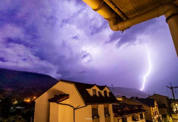 En esta imagen tomada desde la ventana de casa en una tormenta eléctrica de verano se ve de fondo la sierra de Urbasa, en el lado derecho de la imagen se ve un luminoso rayo cayendo sobre ella. En el plano medio se ven los edificios del barrio.